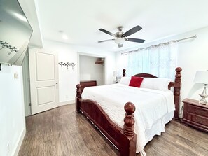 A bedroom with a wooden four-poster bed, a ceiling fan, a bedside table with a lamp, and a window with curtains. - The Fort Worth Overlook (Fort Worth)