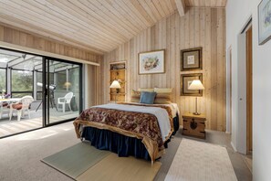 Ein Schlafzimmer mit einem großen Bett, zwei Nachttischlampen, einem Holz-Kopfteil, einer Glastür, die zu einem Außenbereich führt, und einem kleinen Nachttisch.