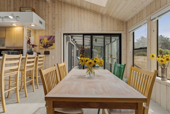 Ein Essbereich mit Holztisch und -stühlen, einer Vase mit Sonnenblumen und Blick durch eine Glastür.