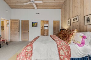 Ein Schlafzimmer mit einem Bett, einem Deckenventilator, Holzwänden und einem Fenster.