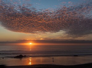 Eine Strandansicht, während die Sonne über dem Ozean untergeht, eine Silhouette einer Person und ein klarer Himmel.
