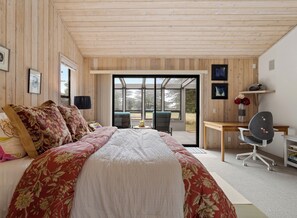 Ein Schlafzimmer mit einem großen Bett, einem Schreibtisch und Blick durch eine Glastür.