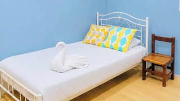 Un lit simple avec un cadre en métal blanc, une chaise en bois et une serviette en forme de cygne.