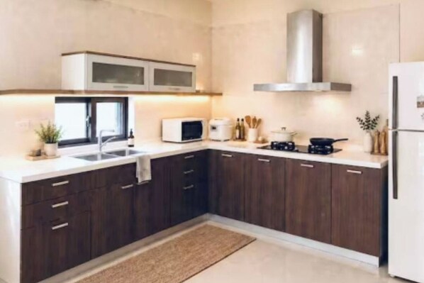 A modern kitchen with dark wood cabinets, a stainless steel range hood, a microwave, and a refrigerator.