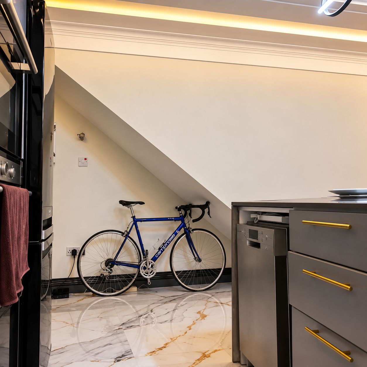 Una cocina con piso de mármol, una bicicleta apoyada en la pared y un mueble gris con tiradores dorados.