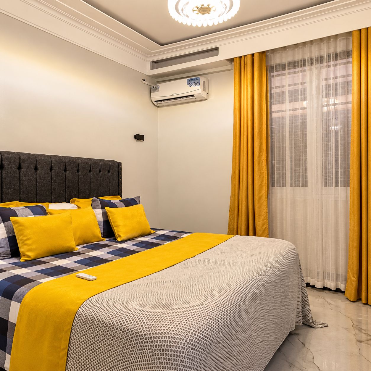 A hotel room with a bed, a wall-mounted air conditioner, and a window with yellow curtains.