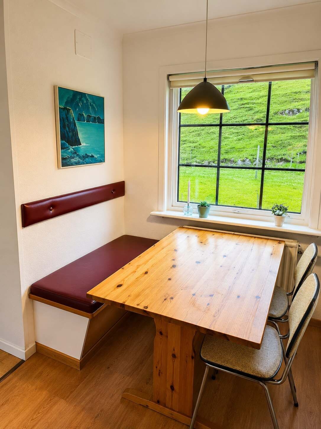 Una habitación con un banco de madera, una mesa y una ventana con vistas a campos verdes.