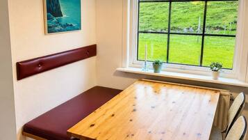 Una habitación con un banco de madera, una mesa y una ventana con vistas a campos verdes.