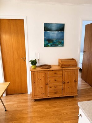 A wooden cabinet with drawers and a shelf, a painting of a seascape, and a potted plant on the cabinet.