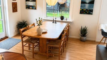 A dining area with a wooden table, chairs, a vase with flowers, and a hanging light fixture.
