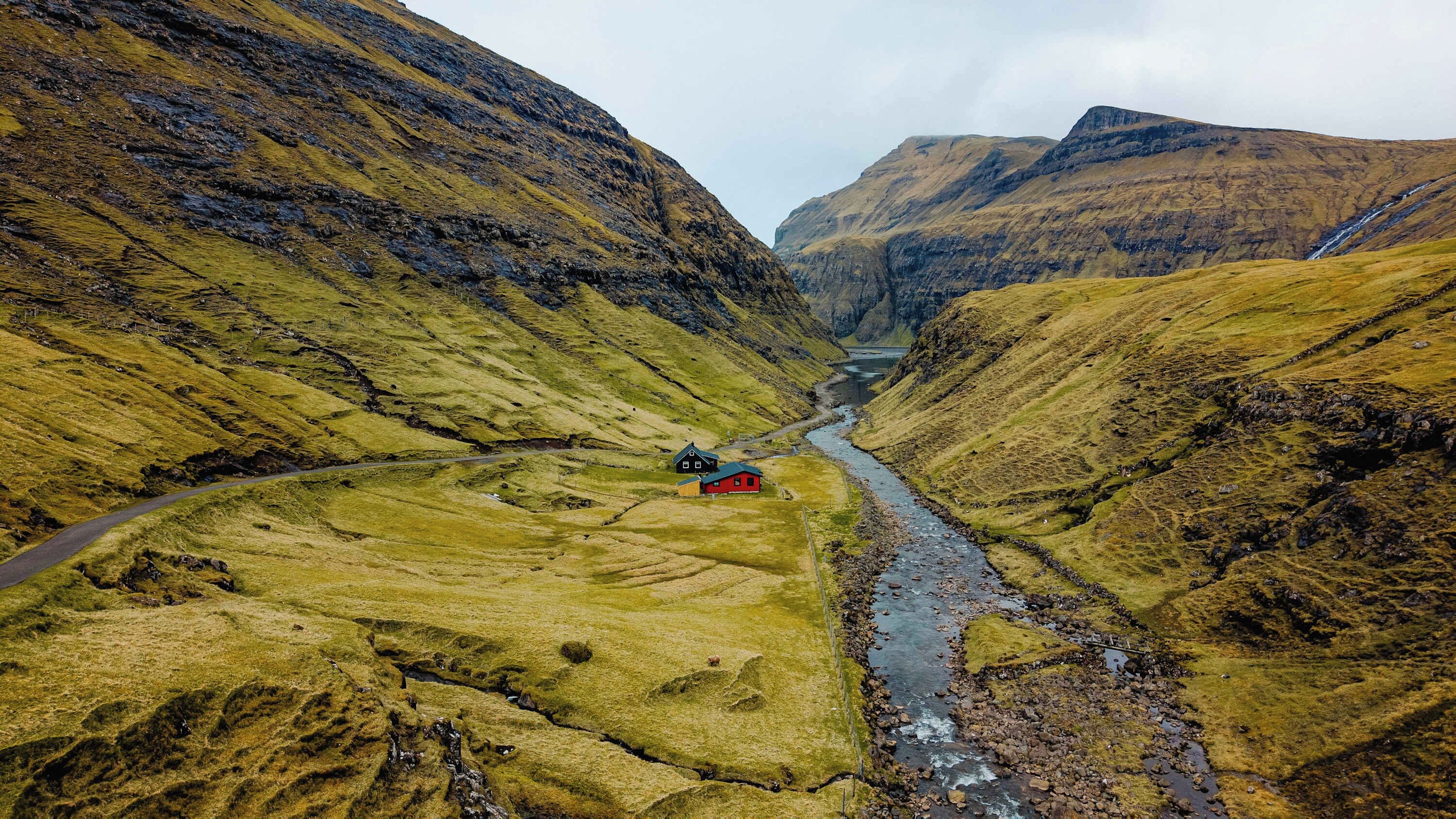 Een afgelegen berglandschap met een smalle vallei, een rivier en een klein huis met een rood dak.