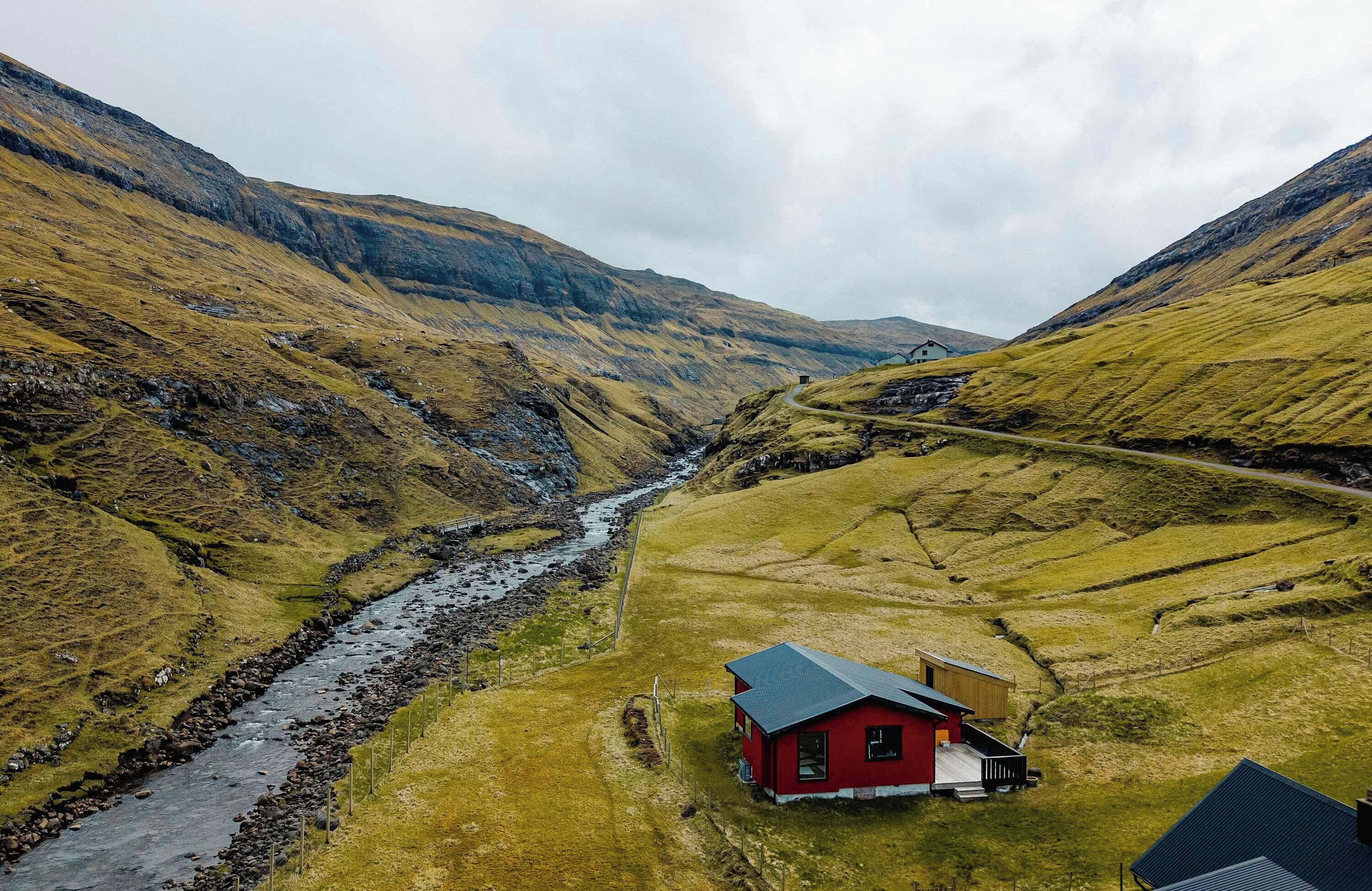 A red building with a sloped roof, surrounded by a valley with a stream, and a road leading up the hill.
