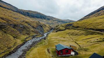 A red building with a sloped roof, surrounded by a valley with a stream, and a road leading up the hill.