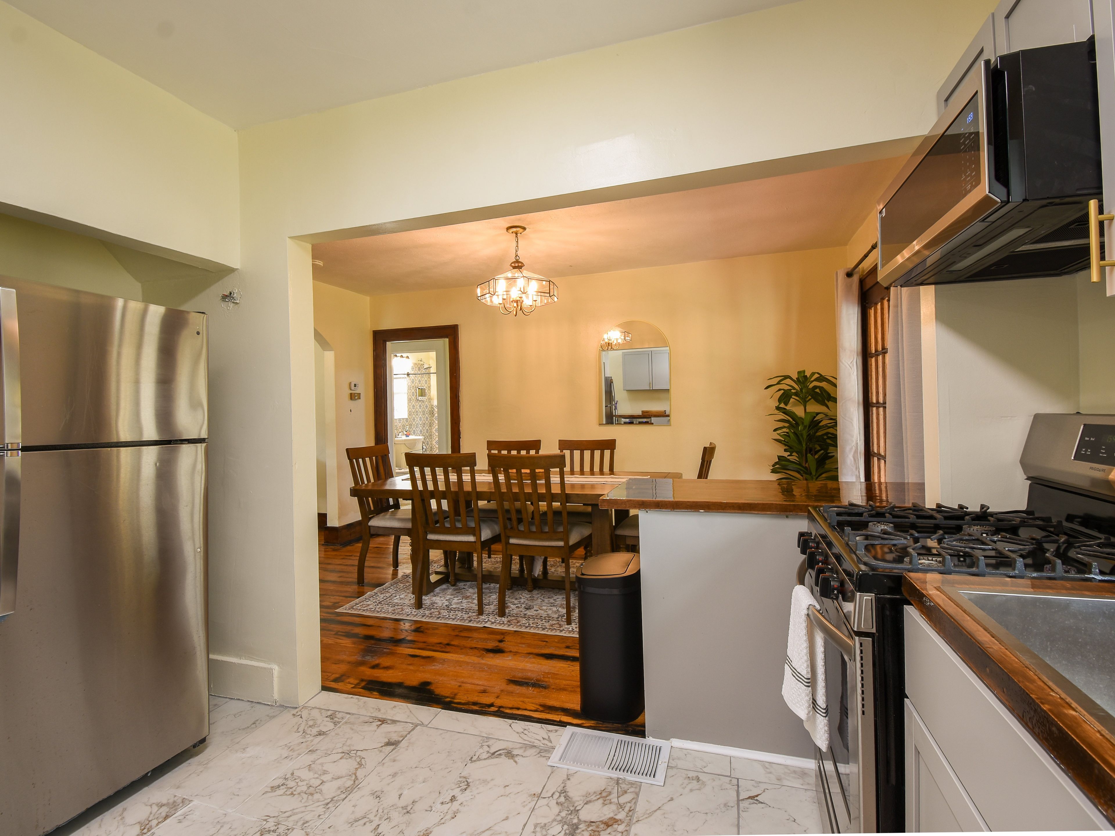 A kitchen with a stainless steel refrigerator, a gas stove, and a dining area with wooden chairs and a chandelier.