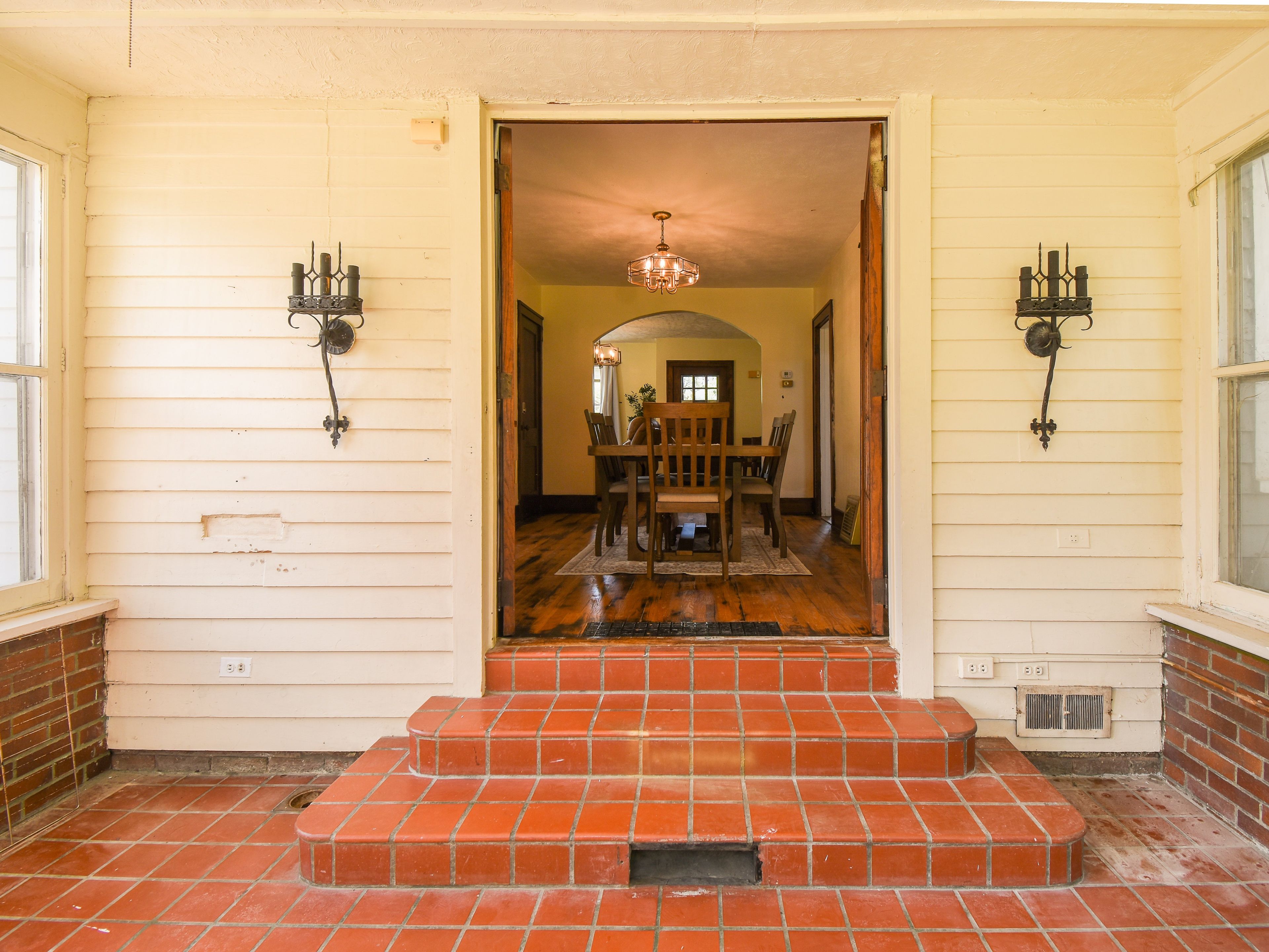 A house entrance with a wooden staircase leading to a dining area with a chandelier.