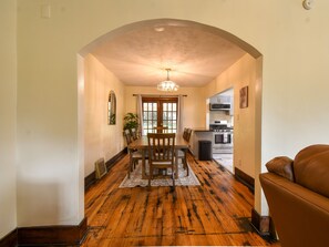 A dining area with a wooden table and chairs, a chandelier, and a view into the kitchen. - Brick Fireplace Central Omaha Family Haven 3 Bedroom Home (Omaha)