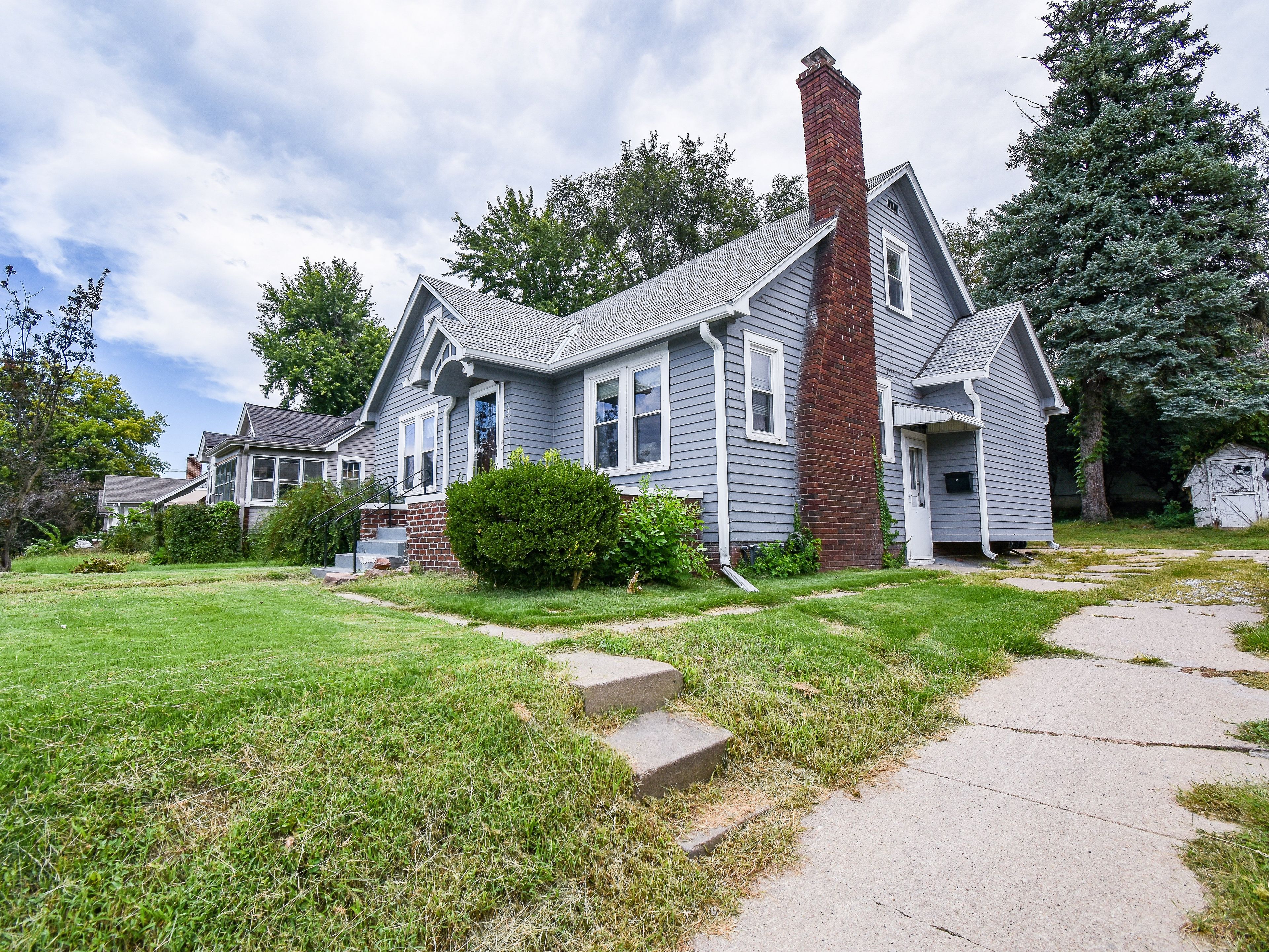 A two-story house with a brick chimney, a front porch, and a well-maintained lawn.