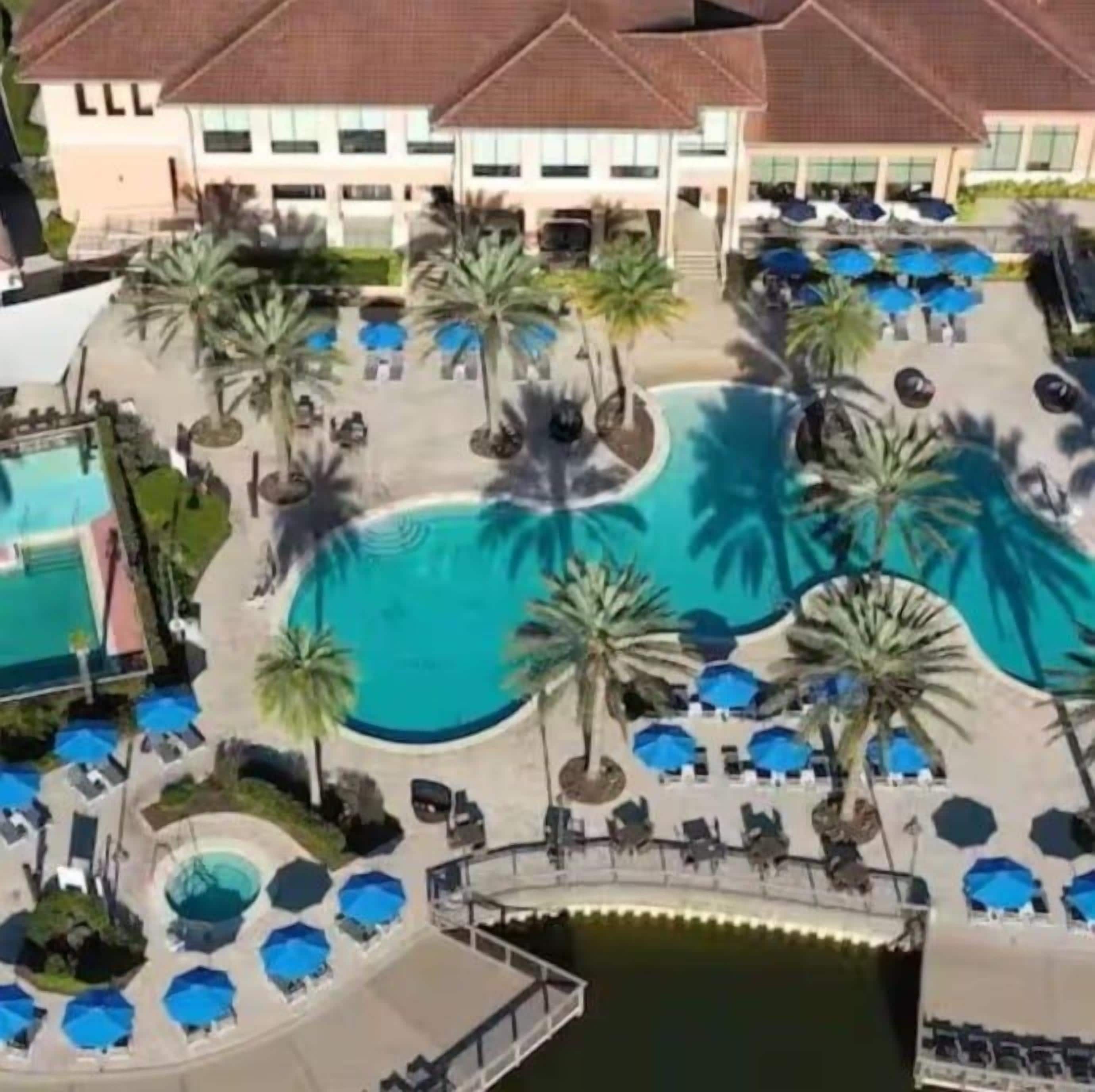 A hotel with a central swimming pool surrounded by palm trees and sun loungers.