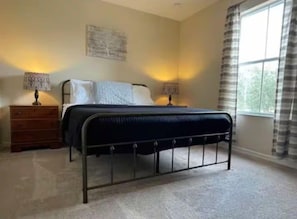 Ein Schlafzimmer mit einem Bett, zwei Nachttischen, einer Kommode und einem Fenster mit Vorhängen.