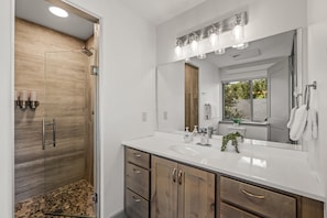 Un baño moderno con ducha a nivel, un espejo grande y un tocador con lavamanos.