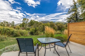 Un patio exterior con mesa y sillas, rodeado de un jardín y vistas a las colinas.