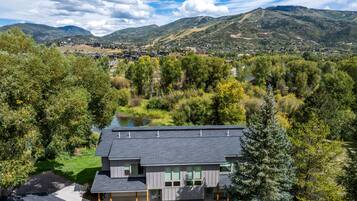 A modern two-story house with a flat roof, surrounded by lush greenery and a lake.