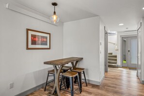 A dining area with a wooden table and bar stools, a pendant light, and a framed picture on the wall.