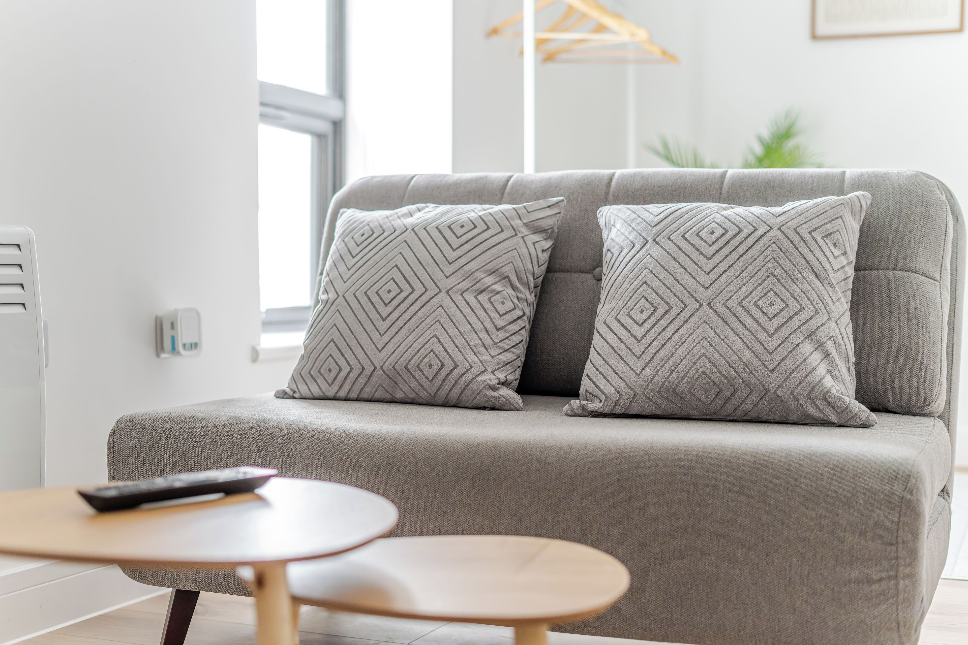 Una sala de estar moderna con un sofá gris, dos cojines estampados, una mesita de madera y un control remoto sobre el sofá.