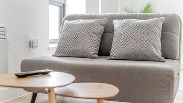 Una sala de estar moderna con un sofá gris, dos cojines estampados, una mesita de madera y un control remoto sobre el sofá.
