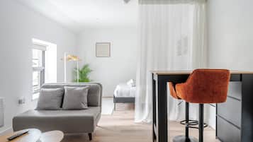A modern living room with a grey sofa, a small round table, a red chair, and a bed in the background.