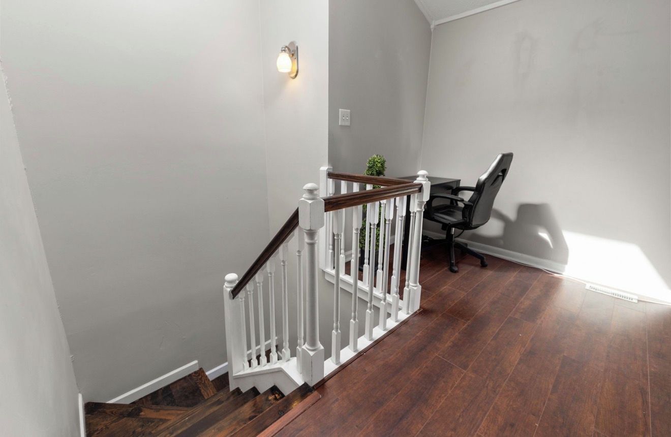 A staircase with white railings and a wooden handrail, leading to a room with a dark wooden floor and a chair.