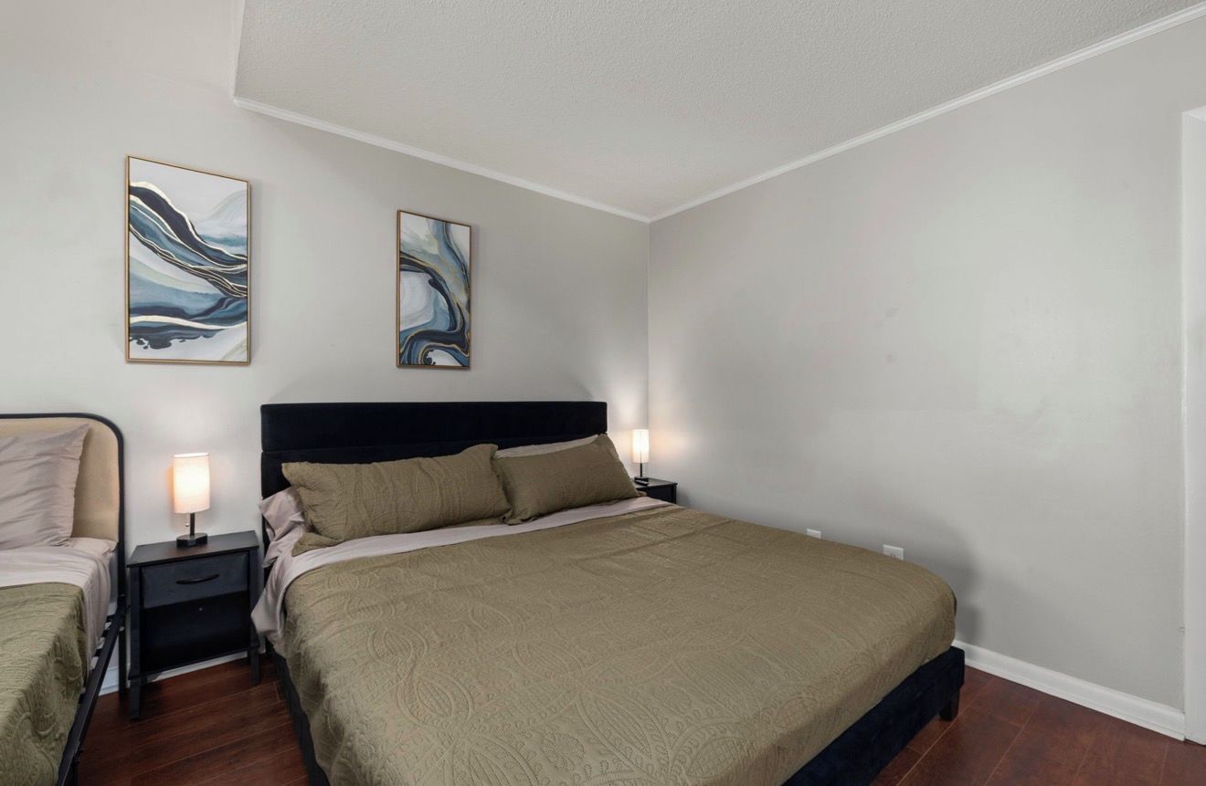 A bedroom with a large bed, two bedside tables with lamps, and abstract wall art.