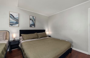A bedroom with a large bed, two bedside tables with lamps, and abstract wall art.