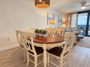 A dining area with a round wooden table and white chairs, a potted plant, and a view of the outdoors. - Orange Beach Condo w/ Indoor & Outdoor Pools (Orange Beach)