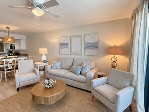 A modern living room with a sofa, armchairs, a coffee table, and a dining area with a chandelier. - Orange Beach Condo w/ Indoor & Outdoor Pools (Orange Beach)