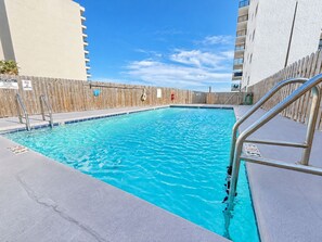 Une piscine entourée d’une clôture en bois, agrémentée de rampes métalliques, et surplombée d’un ciel bleu clair.