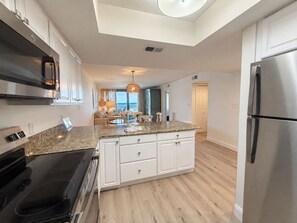 A modern kitchen with a central island, stainless steel appliances, and a view to the living area. - Orange Beach Condo w/ Indoor & Outdoor Pools (Orange Beach)
