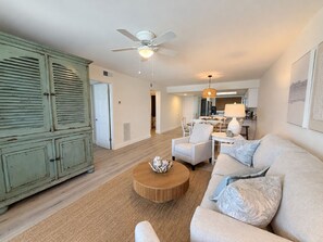 Un salon spacieux avec un plafond haut, un ventilateur de plafond, une table basse ronde, un canapé et un coin repas à l’arrière-plan.