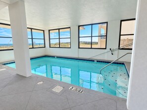 An indoor swimming pool with clear blue water, a diving board, and large windows offering views of the beach. - Orange Beach Condo w/ Indoor & Outdoor Pools (Orange Beach)