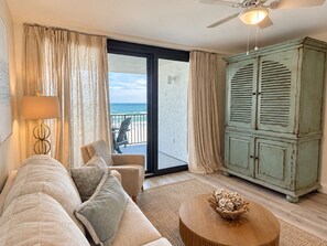 A living room with a sofa, armchairs, a coffee table, a cabinet, and a view of the sea through a sliding door. - Orange Beach Condo w/ Indoor & Outdoor Pools (Orange Beach)