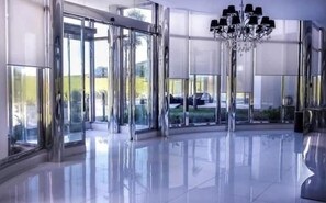 A modern lobby with a glass revolving door, a chandelier, and a reflective floor.