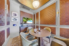 Um quarto com uma mesa redonda, duas cadeiras, uma televisão e um painel decorativo na parede.