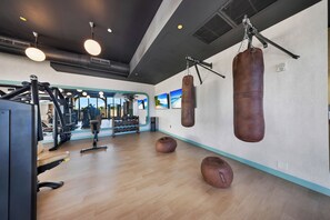 Uma academia com equipamentos de ginástica, sacos de pancada e um espelho refletindo o ambiente.
