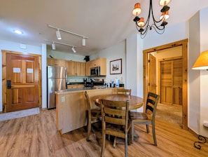 A kitchen with wooden cabinets, a stainless steel refrigerator, a microwave, and a dining area with a wooden table and chairs. - Pool View| Walk to Slopes, Dining, Shops (Keystone)