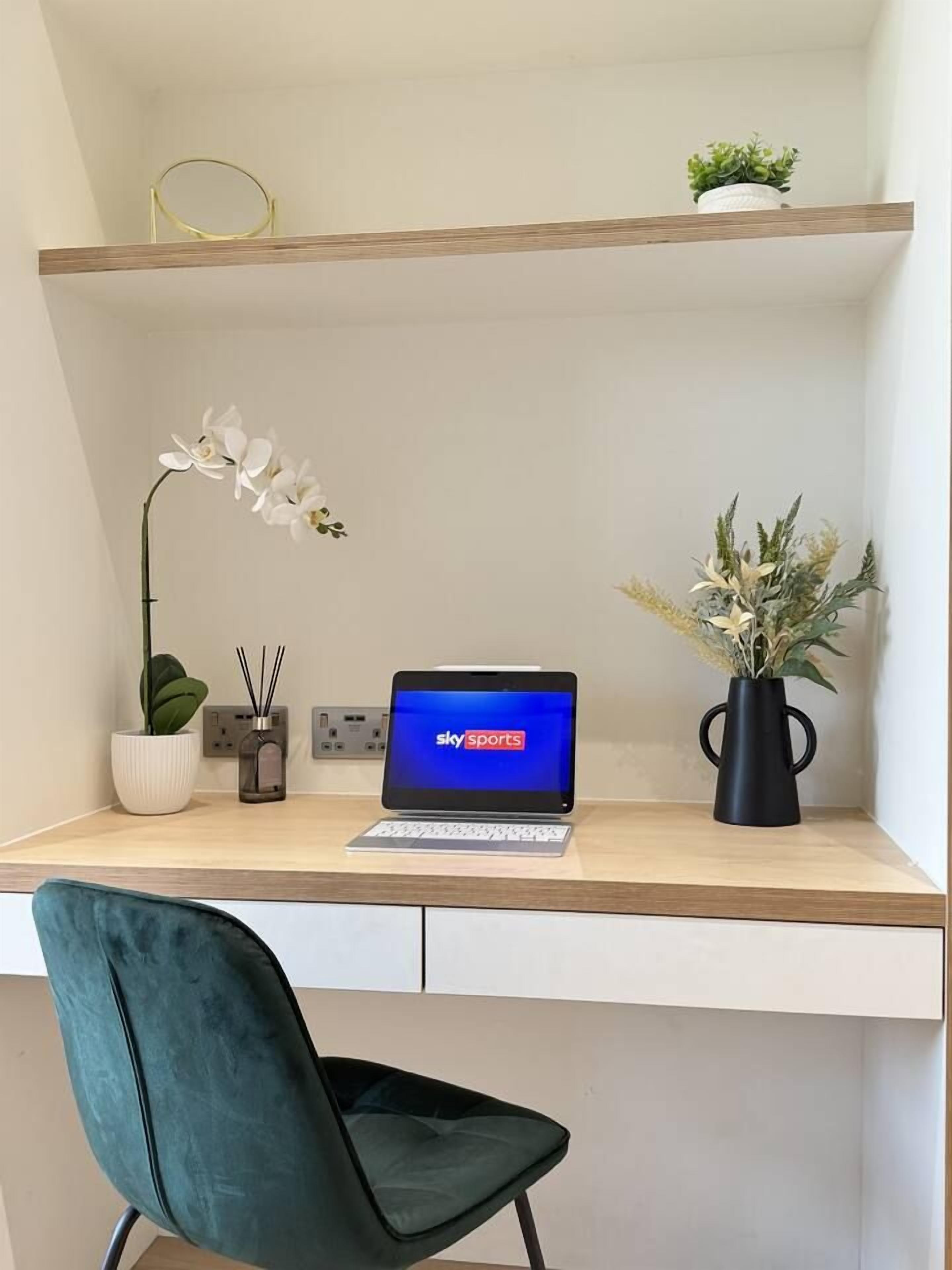 Um espaço de trabalho com um laptop em uma mesa, uma planta em vaso e um vaso com flores.