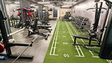 A gym with various exercise equipment, green turf flooring, and weightlifting stations.