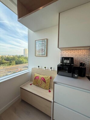 A compact room with a window, a sofa with a decorative pillow, a microwave, and a framed poster on the wall.