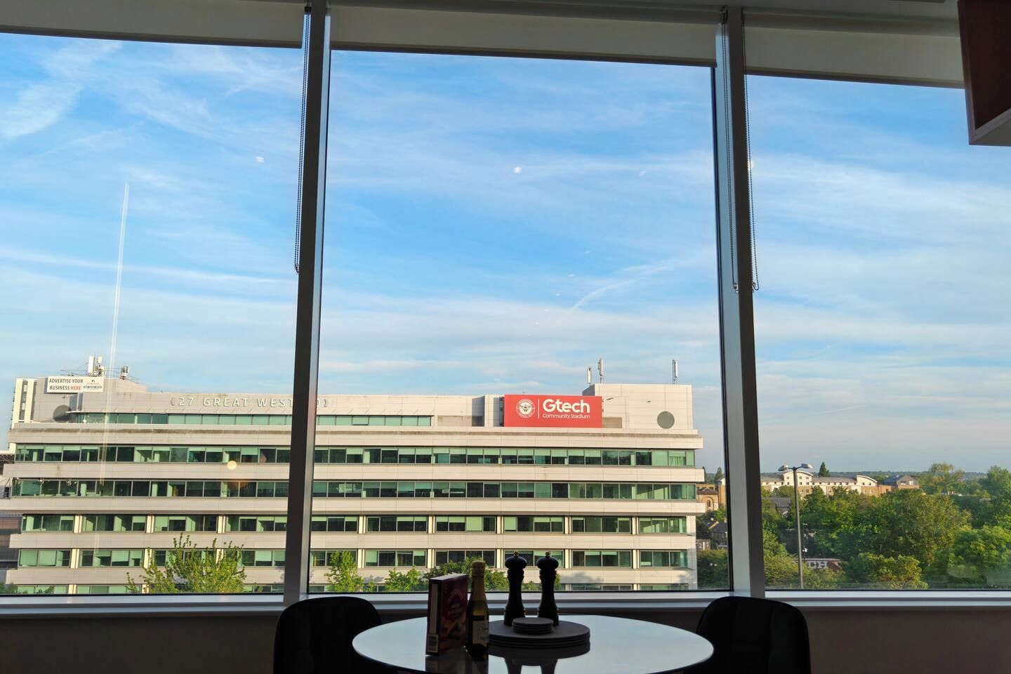 A view from a window with a table and chairs, overlooking a building with a sign reading 'Gtech Community Stadium.'