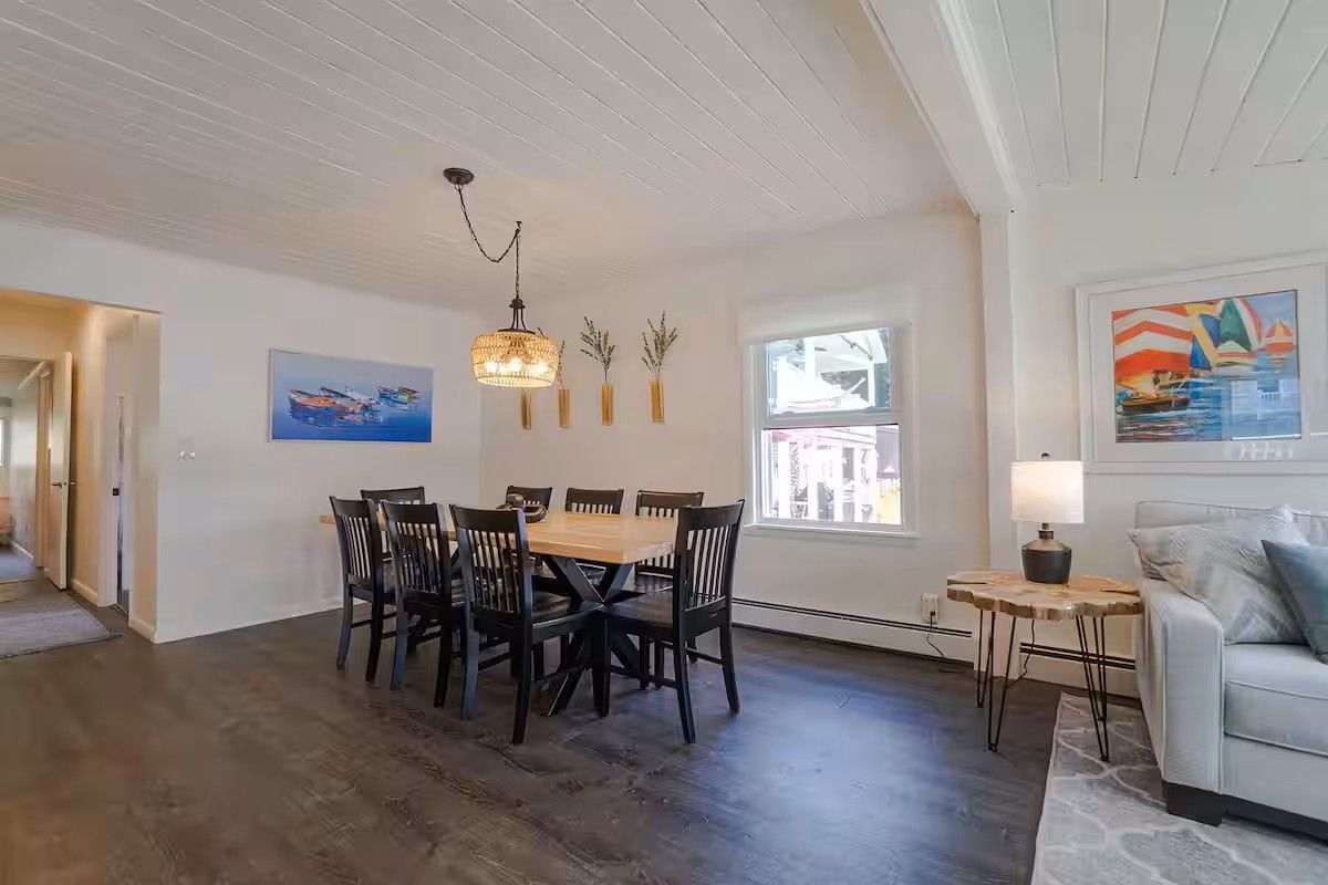 A dining area with a wooden table and chairs, a hanging light fixture, and a window with a view.