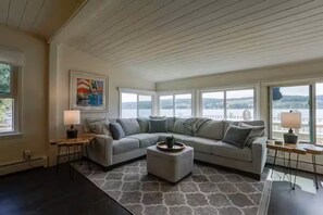 A living room with a sectional sofa, a coffee table, and a view of the outdoors through large windows.